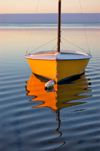 A yellow dory glowing at golden hour, mirrored on still water
