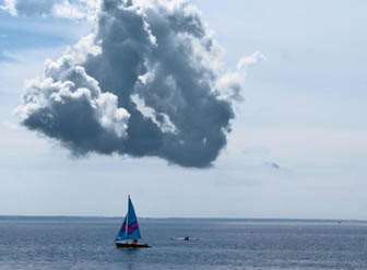 A sailboat under a towering cloud at midday on the bay